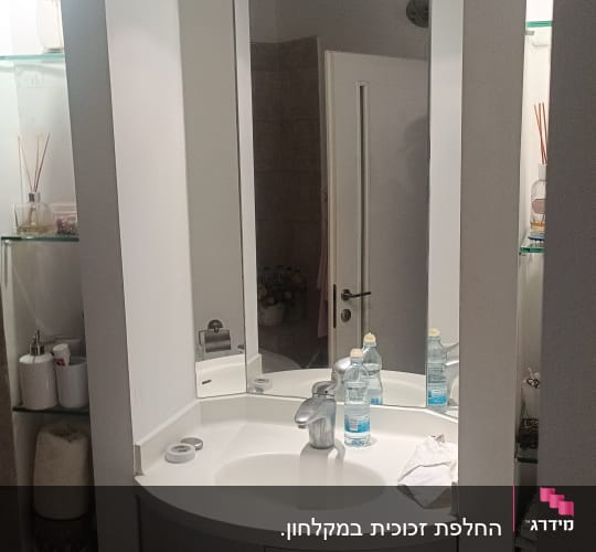 מראה גדולה מעל כיור עם בקבוקי מים